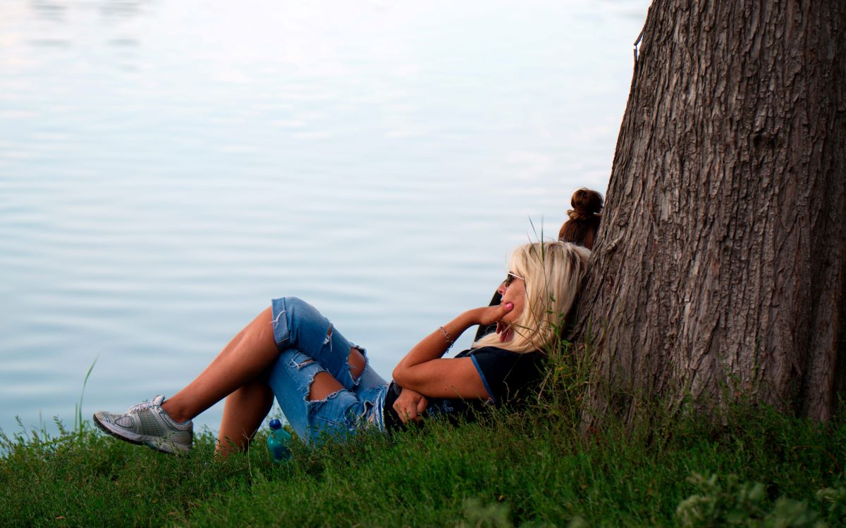 femme assise près d'un arbre au bord de l'eau dans l'état de lâcher prise 